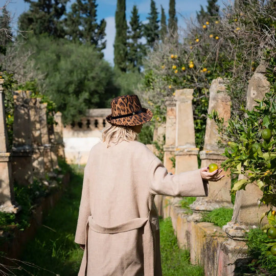 cappello a cloche asimmetrica animalier in feltro di lana merinos primario nesti modella con cappotto beige ambientazione giardino allitaliana con colonne antiche