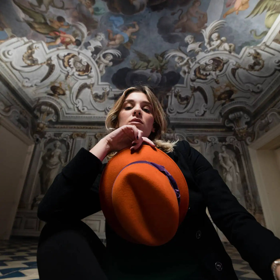 cappello a cloche con corona incavata a tesa corta primario nesti arancio primo piano modella su sfondo architettonico stile retro contemporaneo