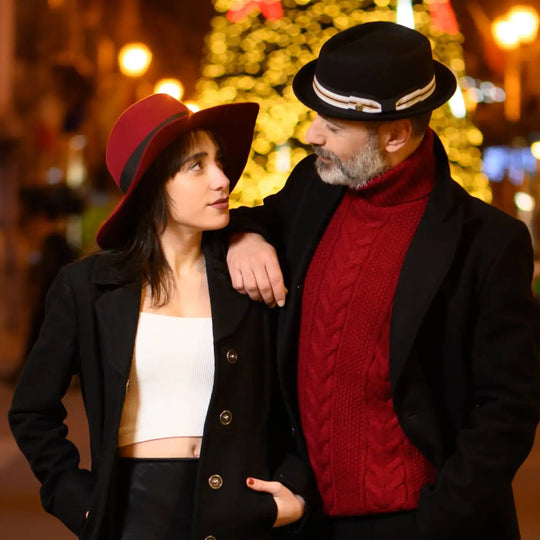 coppia elegante con cappello tesa a taglio vivo in feltro di lana merinos antipioggia rosso rubino e cappello pork pie nero primario nesti atmosfera natalizia