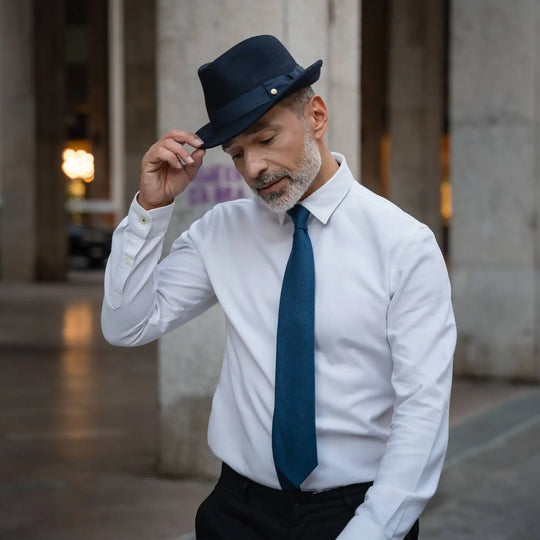 gentleman con trilby classico primario nesti lapin blu navy camicia bianca e cravatta azzurra gesto elegante sotto i portici