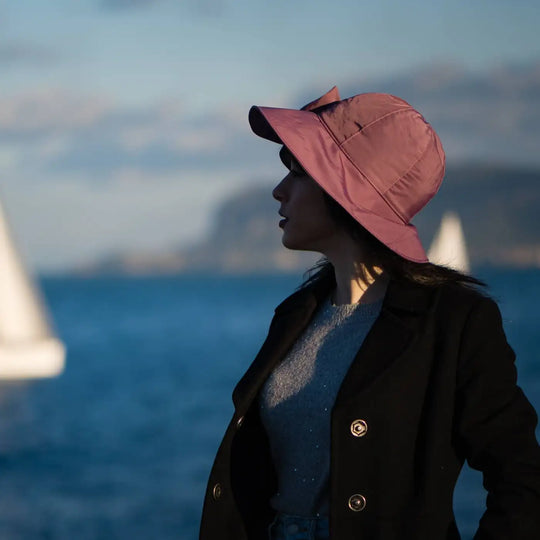 modella con bucket impermeabile foderato in pile con fiocco primario nesti colore malva tramonto sul mare e barca sullo sfondo