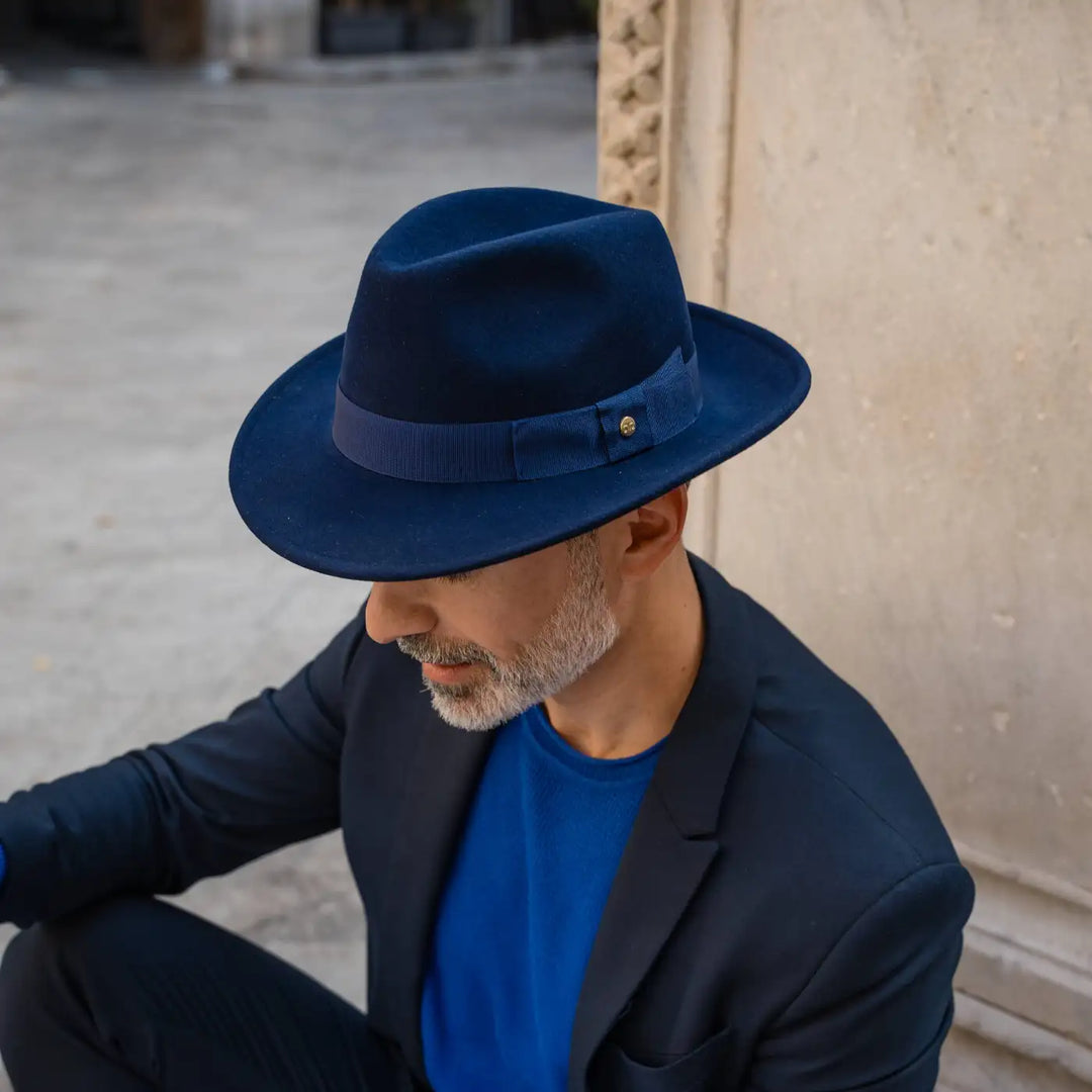 modello adulto con barba curata indossa un cappello fedora in feltro di morbido cashmere primario nesti blu nel suo look business casual legge una rivista