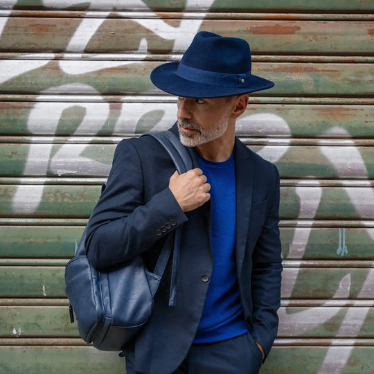 modello adulto con cappello fedora in feltro di morbido cashmere blu primario nesti in posa urbana davanti ai graffiti