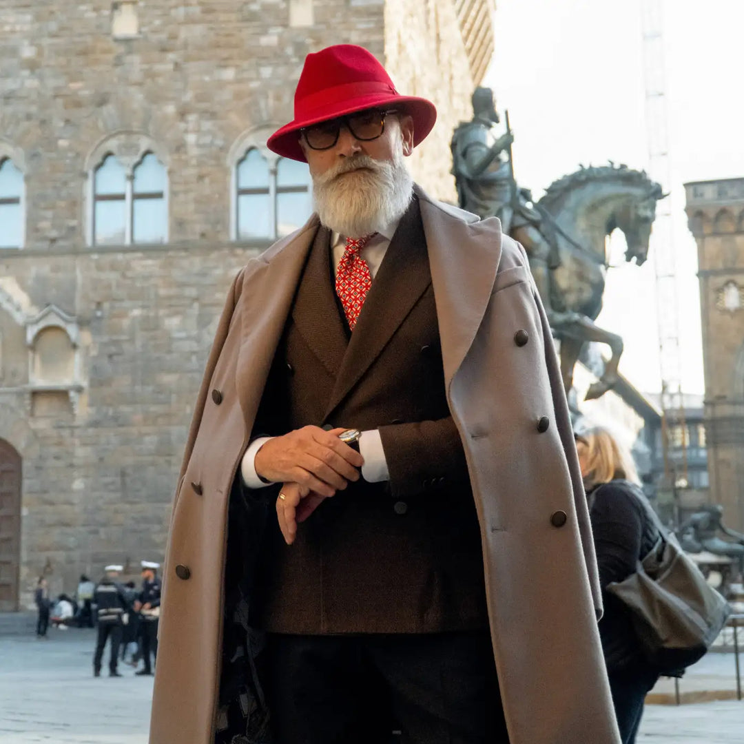 modello distinto con cappello indiana jones primario nesti in lana merinos rosso nel suo outfit formale con cappotto e location storica fiorentina per u