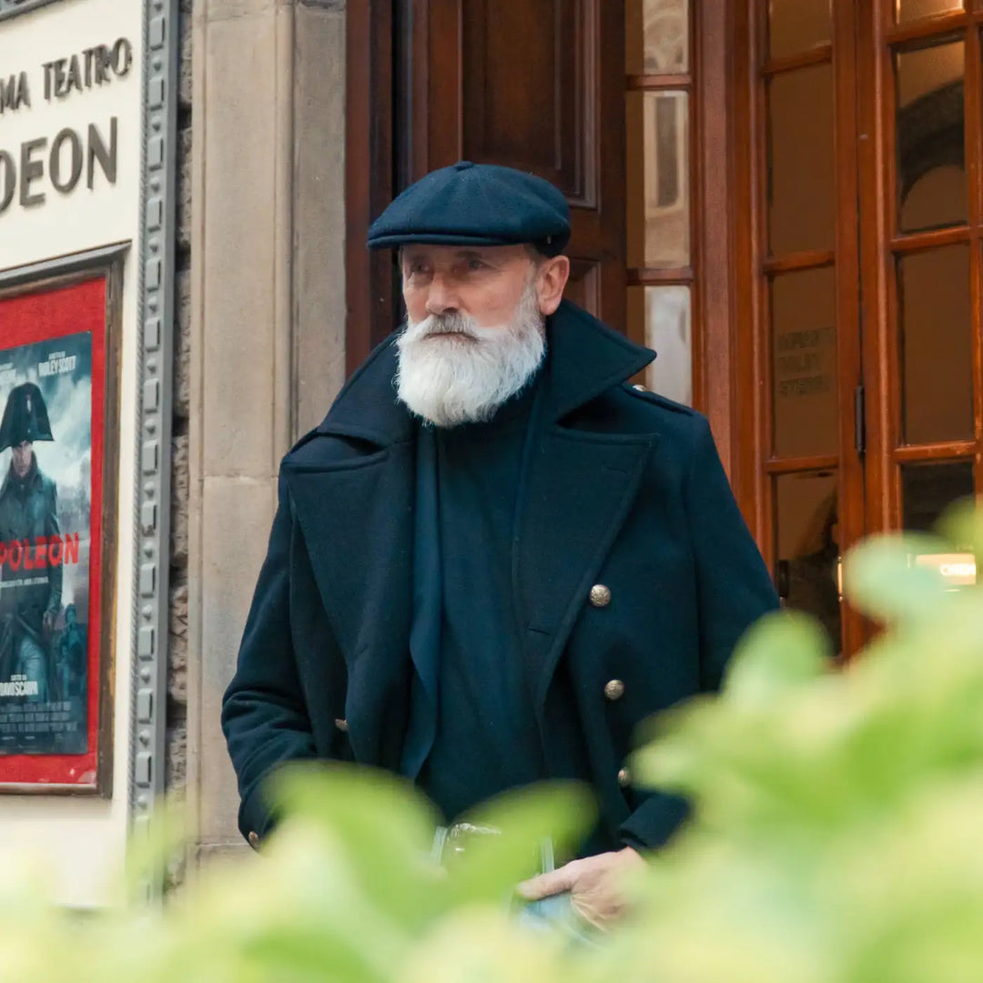 modello distinto con coppola peaky blinders primario nesti blu nel suo outfit invernale scuro e ambientazione negozio storico con elementi naturali