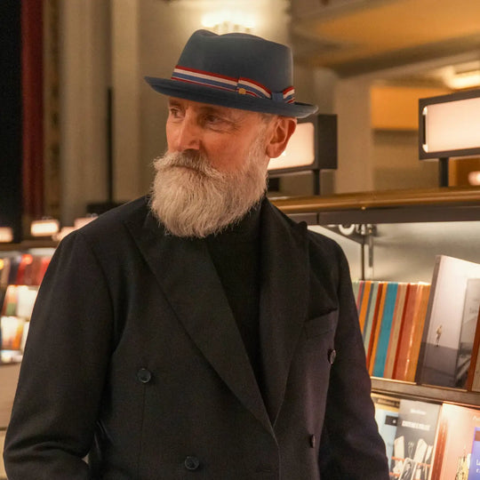 modello elegante con cappello pork pie primario nesti in lana merinos colore carta zucchero in un ritratto suggestivo tra gli scaffali di libreria storica fiorentina