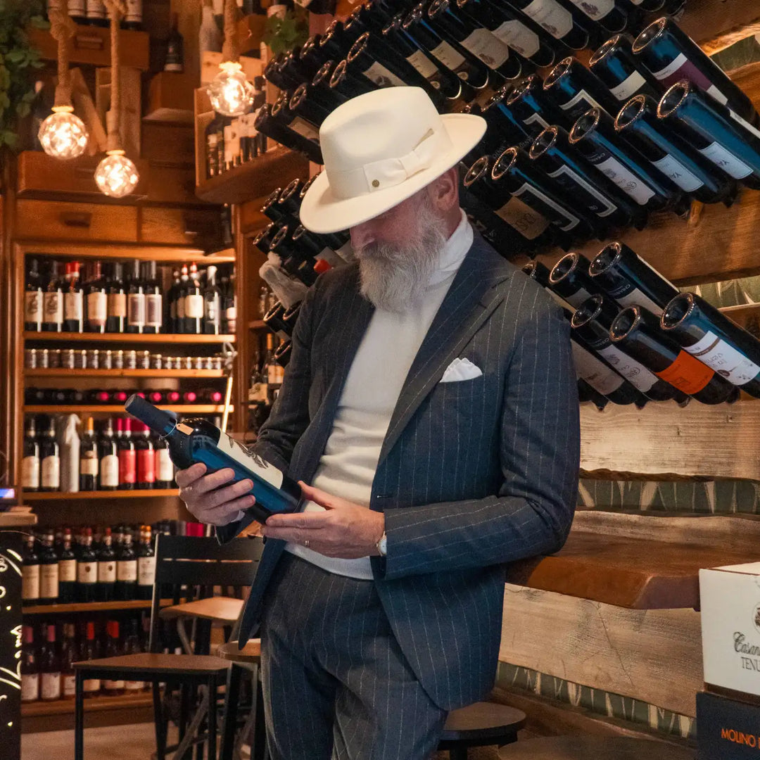 modello maturo con barba curata indossa cappello fedora coccos primario nesti colore bianco panna in enoteca con un outfit invernale sofisticato atmosf