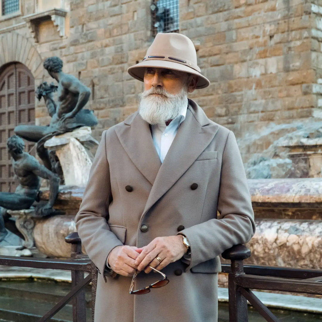 modello maturo con cappello fedora tesa corta primario nesti antipioggia colore beige indossa un completo beige scuro per uno stile italiano raffinato tra colonne storiche