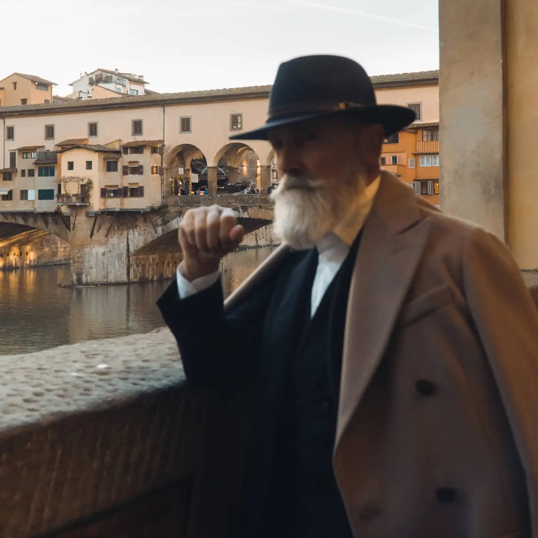 modello maturo con cappello fedora tradizionale primario nesti antipioggia blu con vista ponte vecchio nel suo look formale invernale e atmosfera fiorentina