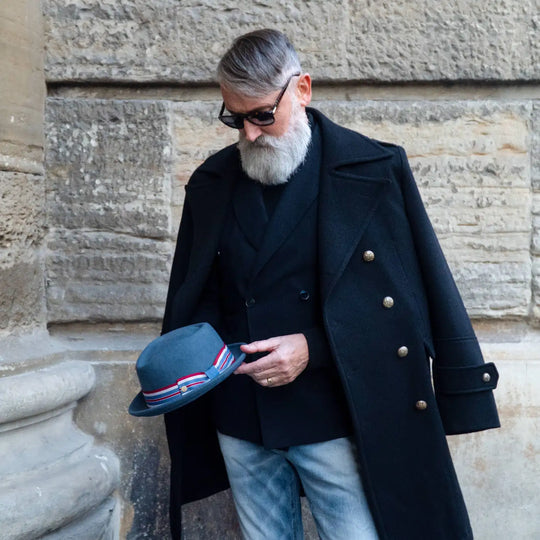 modello maturo con cappello pork pie primario nesti in lana merinos nel suo look casual chic con cappotto lungo e jeans un eleganza urbana sullo sfondo