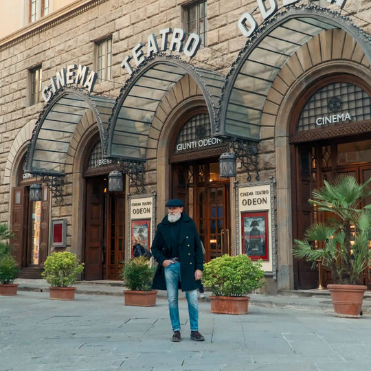 modello maturo con coppola peaky blinders primario nesti blu nella sua inquadratura ampia davanti negozio storico con archi