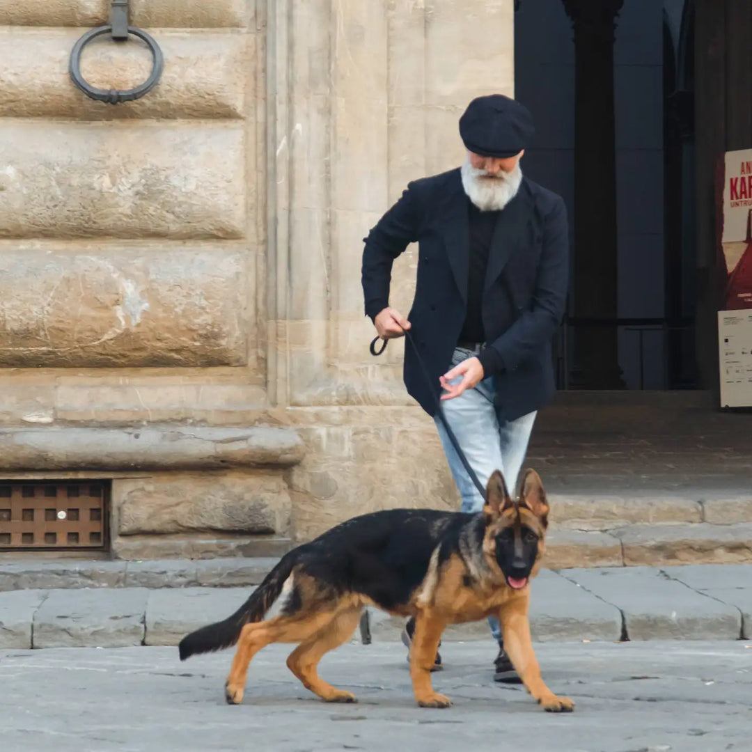 modello maturo con coppola peaky blinders primario nesti blu passeggi con cane nel suo outfit casual urbano in location storica fiorentina