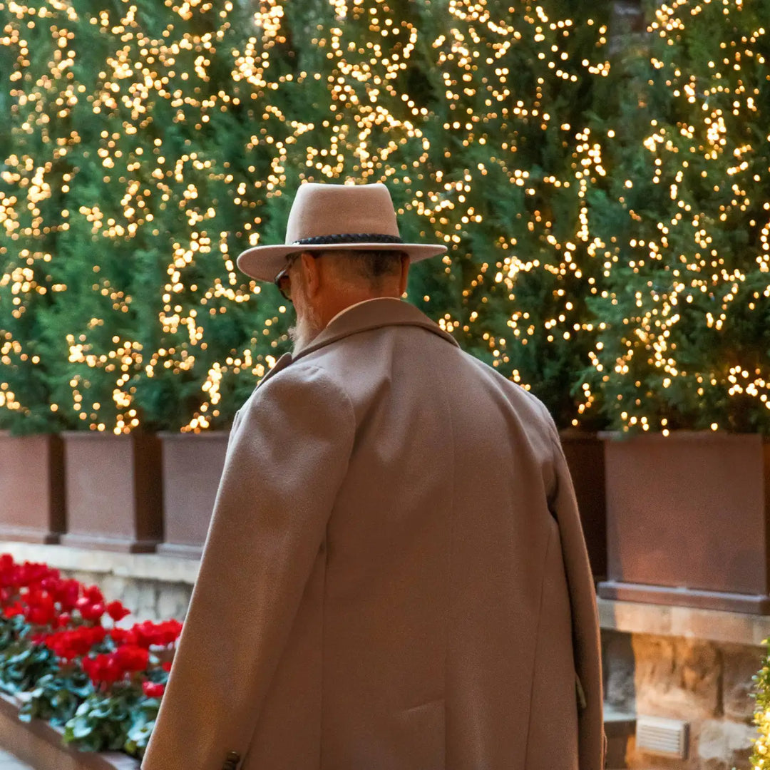 modello maturo sofisticato con cappello fedora australiano primario nesti antipioggia indossa un look invernale elegante con scenario natalizio e fiori rossi