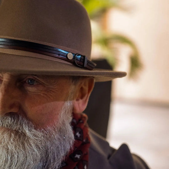 modello sofisticato con cappello fedora classico primario nesti antipioggia dettaglio profilo con barba curata e piante sullo sfondo