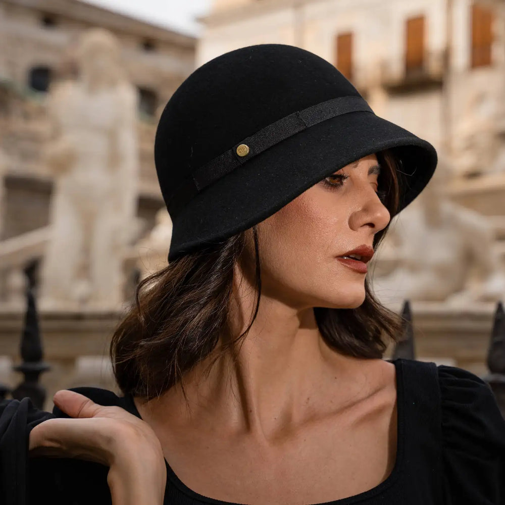primo piano laterale di modella adulta con cappello a cloche signorile a tesa media primario nesti nero e dettaglio architettonico barocco