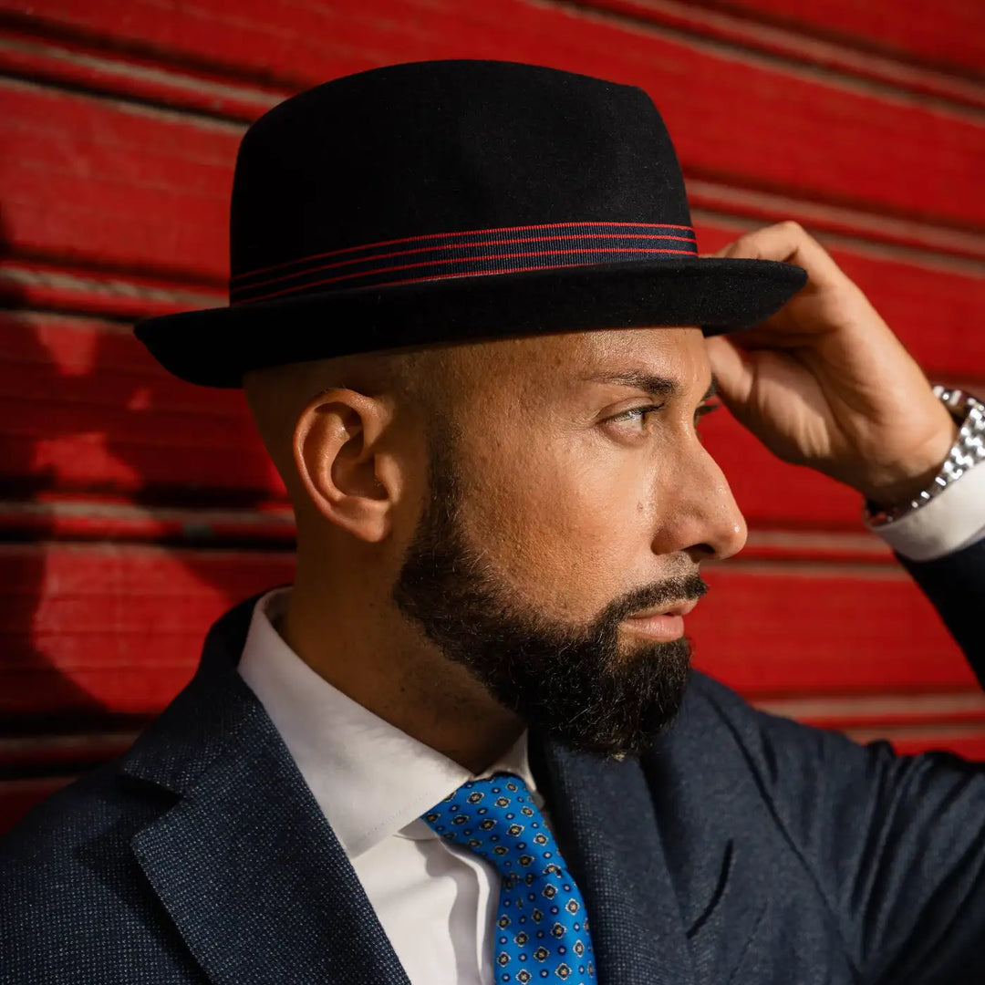 primo piano laterale modello adulto con cappello lobbia homburg in feltro raso di lapin primario nesti che tocca la tesa sfondo rosso industriale