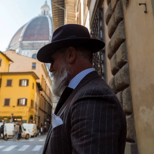 profilo di modello maturo con barba bianca indossa un cappello fedora coccos primario nesti in lana merinos colore marrone sfoggiando una moda italiana nel centro storico