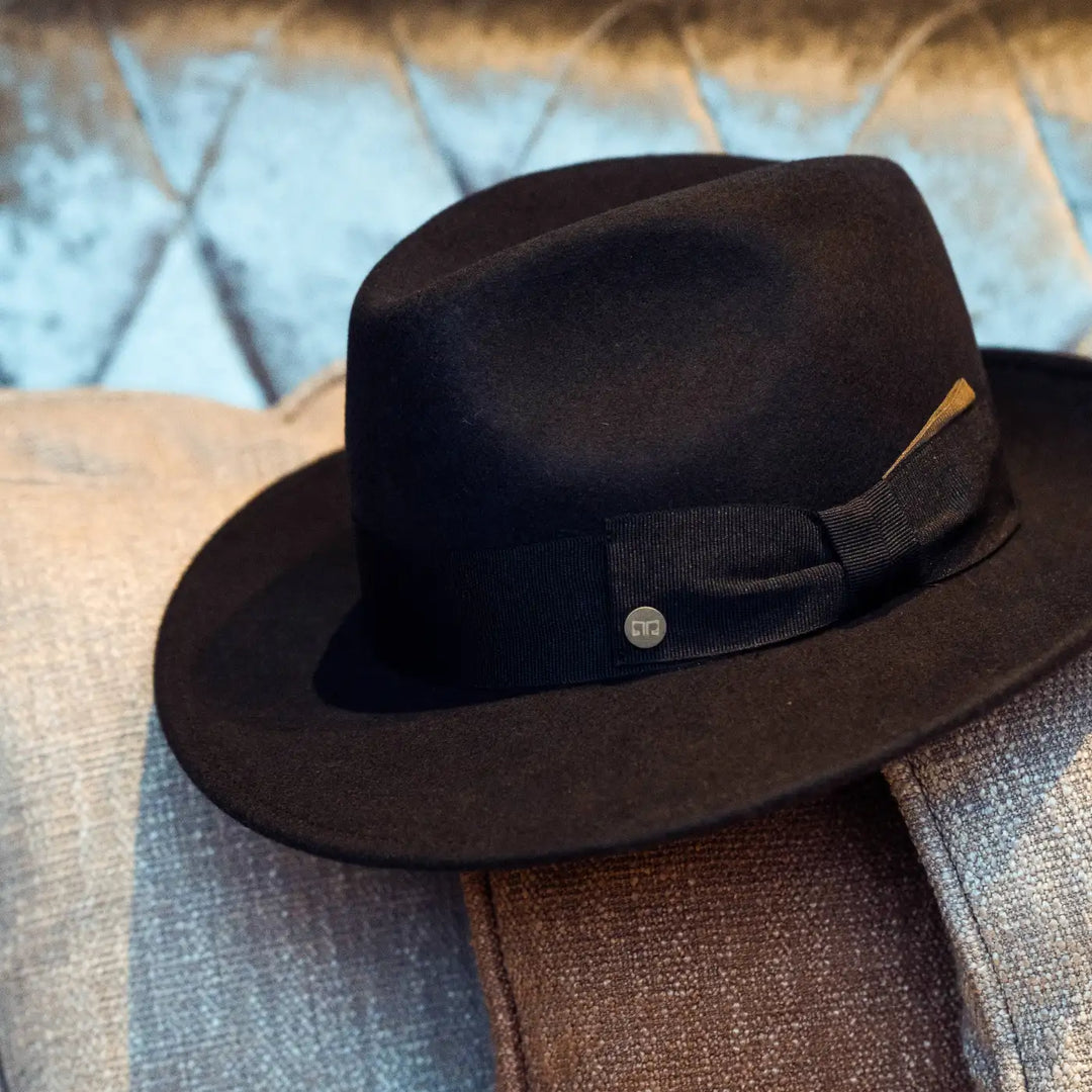 still life cappello fedora coccos primario nesti in lana merinos colore marrone su composizione di tessuti pregiati e dettagli sartoriali