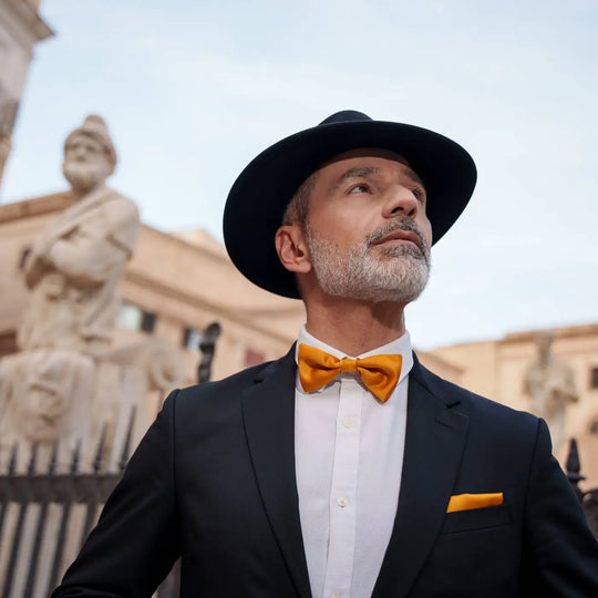uomo distinto con cappello fedora primario nesti cashmere antipioggia nero ritratto controluce dettagli papillon arancio
