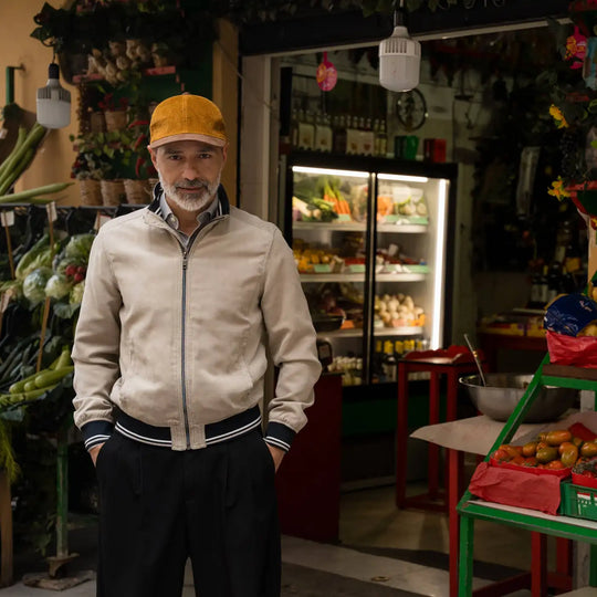 uomo elegante con berretto primario nesti velluto ocra ambientazione mercato frutta colori vivaci