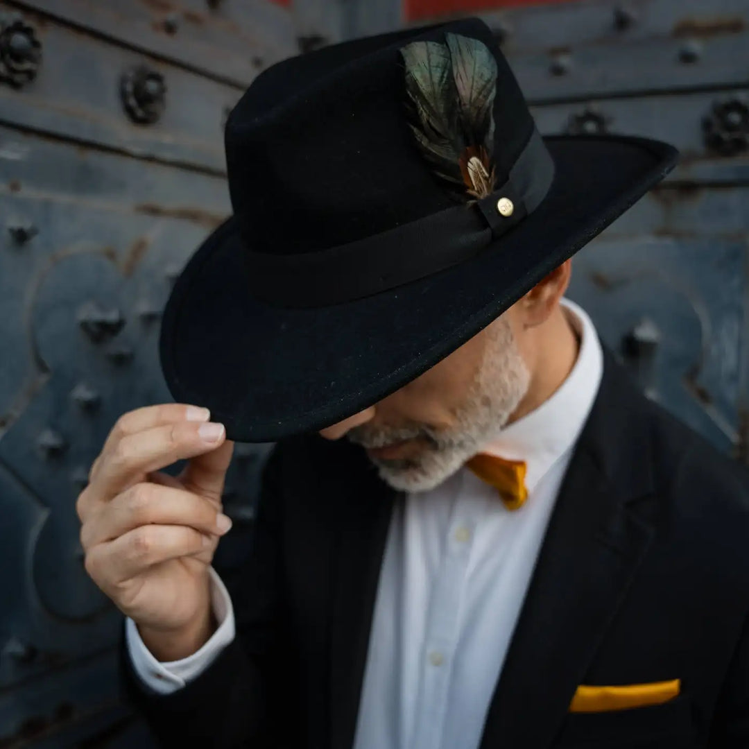 uomo elegante con cappello australiano primario nesti cashmere nero gesto sicuro dettaglio papillon arancio su bianco atmosfera vintage